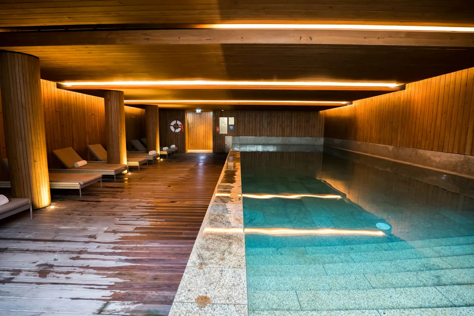 Indoor swimming pool with wooden walls and lounge chairs.